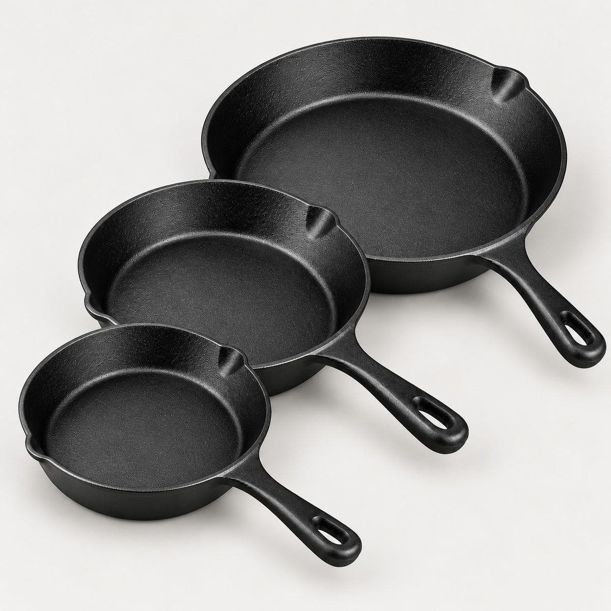 Three pre-seasoned cast iron skillets, 16, 20 and 26 cm, in a staggered row