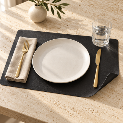 Black reversible faux leather placemat on a travertine table, corner curled to show the smooth black back