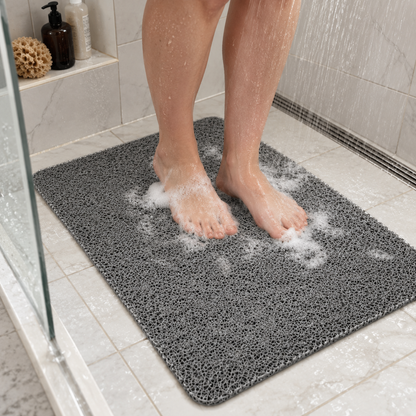 Feet standing on a gray loofah shower mat in a walk-in shower